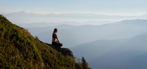 Sporty young woman meditating in mountains.